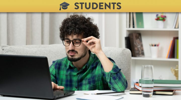 Student with afro and glasses looking at a laptop puzzled