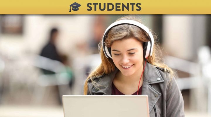 Casual girl listening music with headphones and searching songs in a laptop sitting on a bench in the street