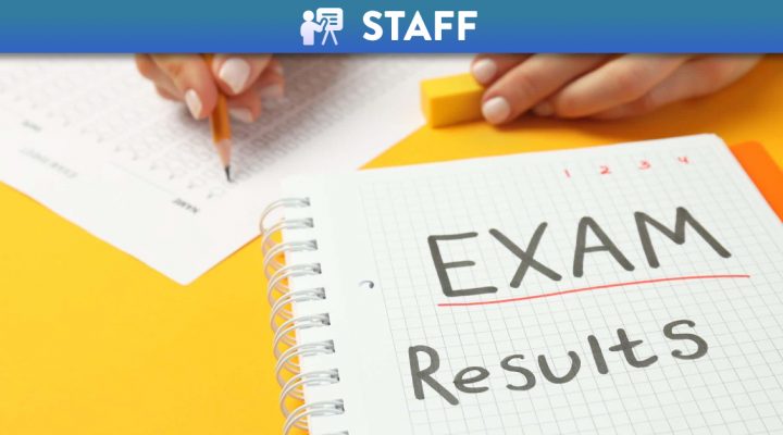 Exam results written on a notebook with hands writing on an exam paper