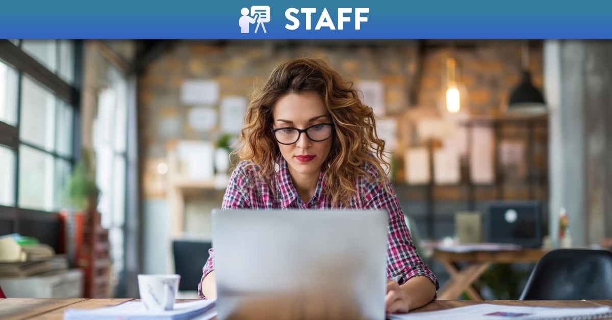 Woman with curly hair and glasses using a laptop in an open office