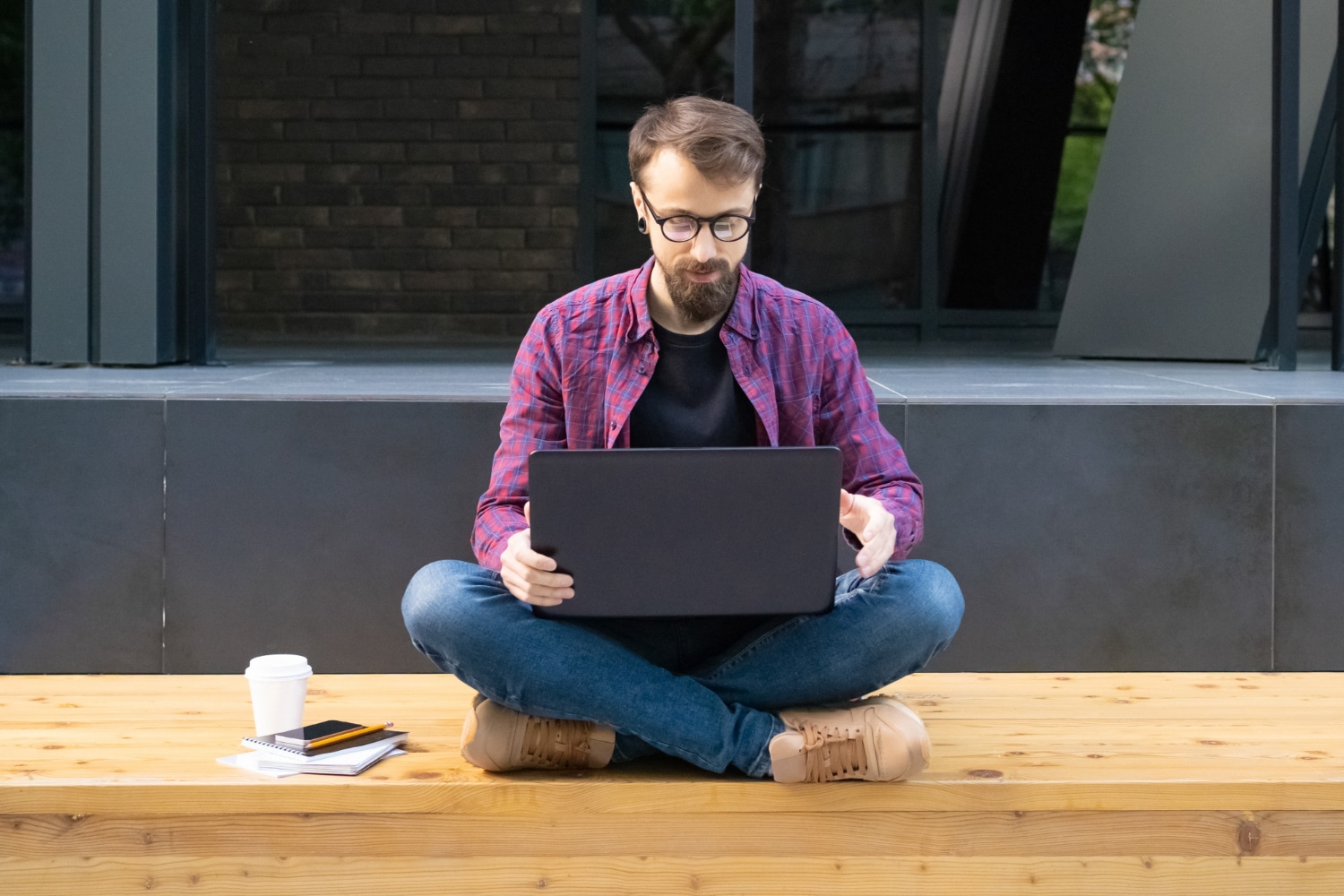Male with glasses sitting cross-legged working on laptop